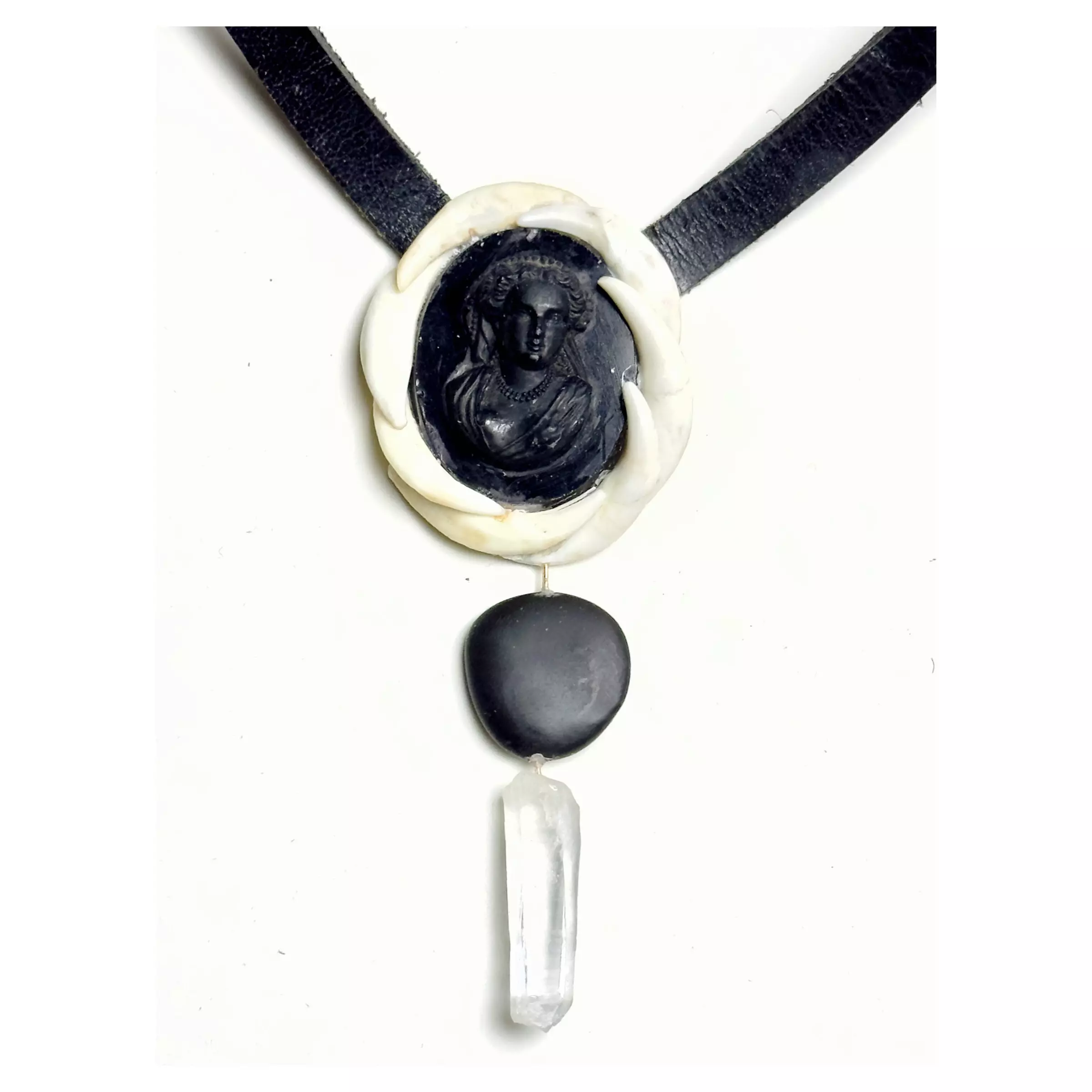 Close-up of a necklace with a black oval carved pendant, a white circular ring around it, and a hanging clear crystal pendant on a white background.